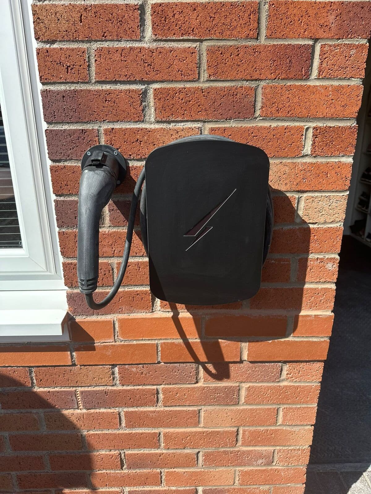 Black home car charger fitted on a red brick wall beside a window