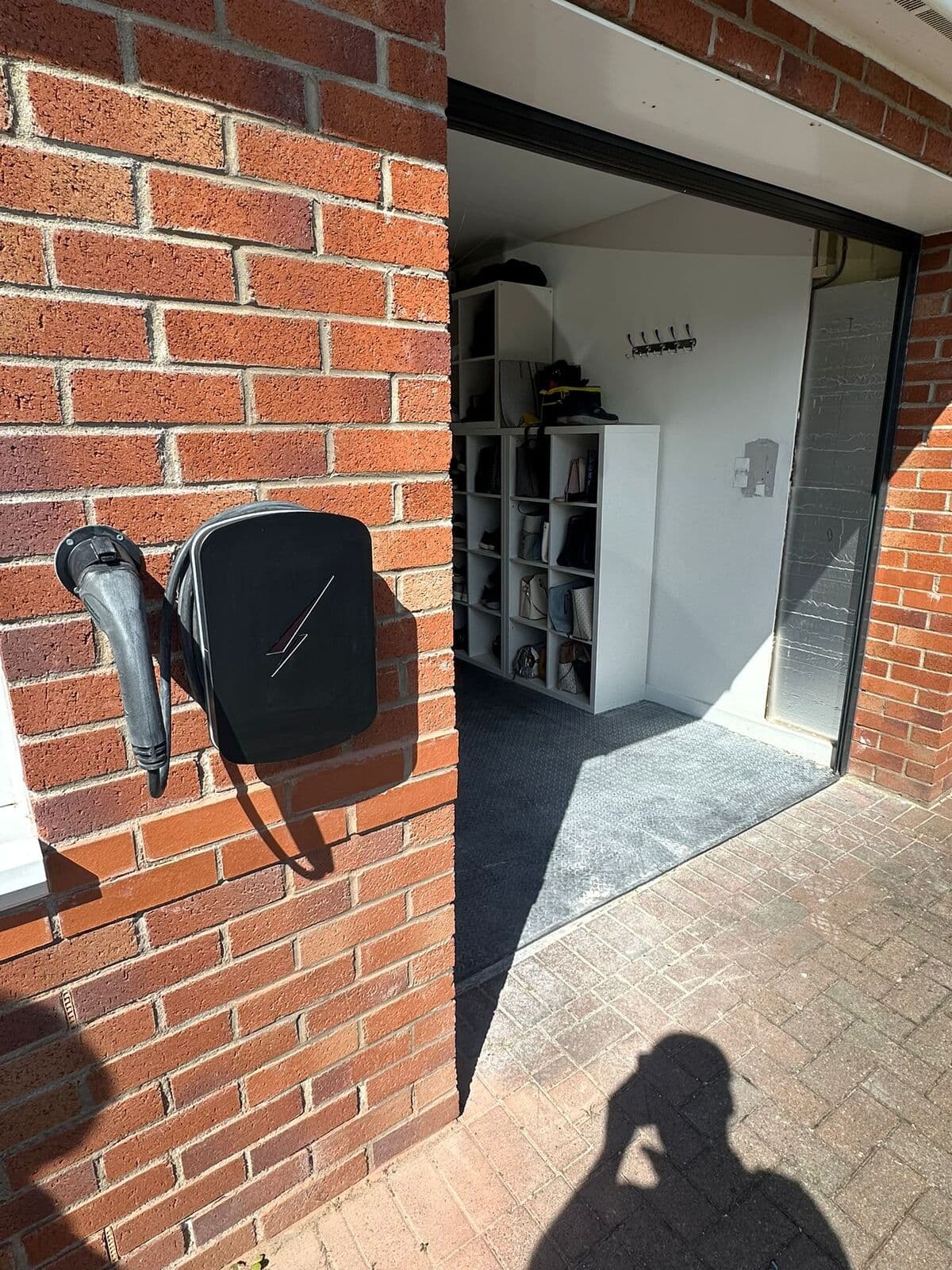 Black car charger fitted on a brick wall beside a garage door