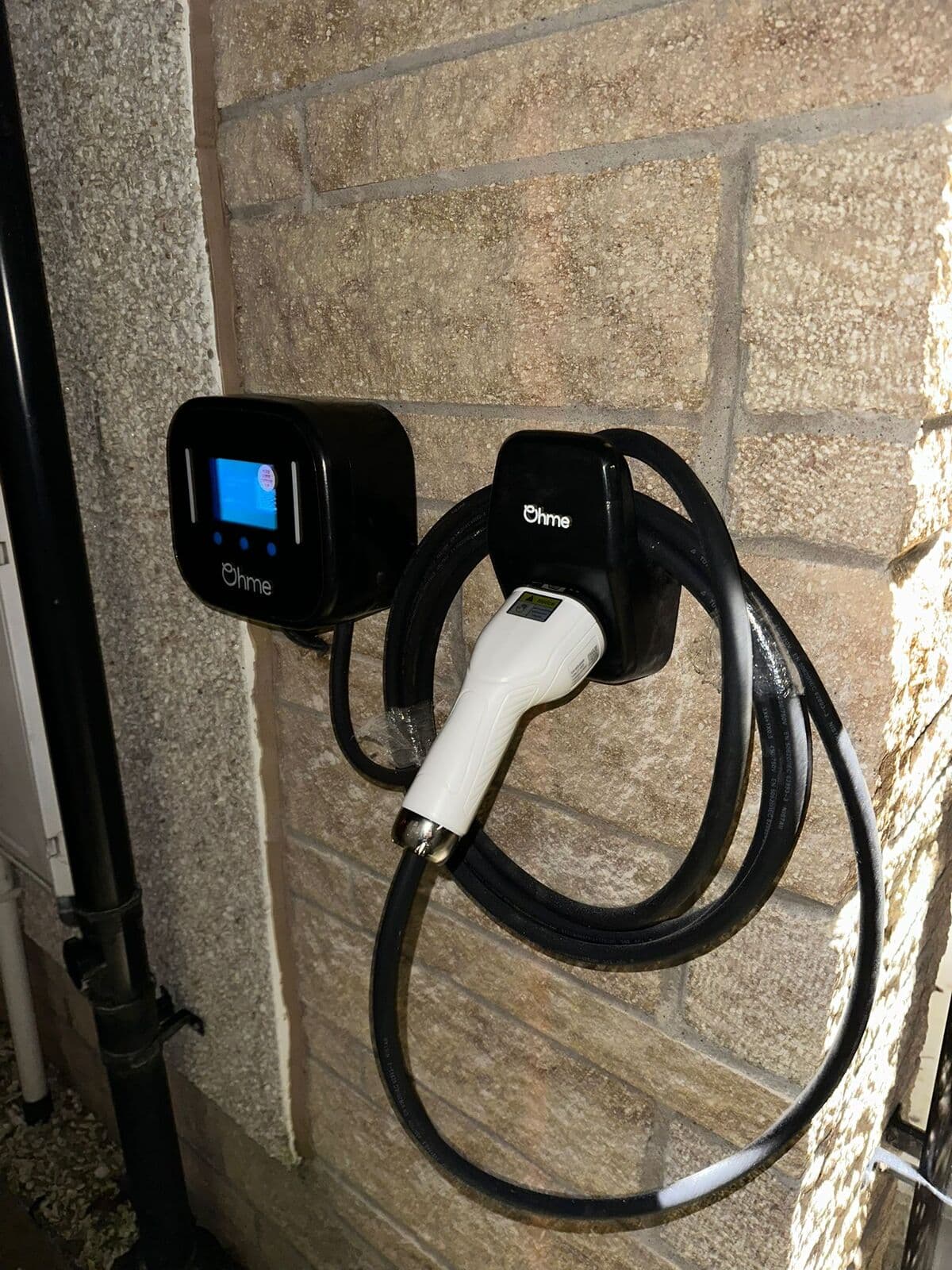 Black Ohme car charger with its cable coiled on a sandstone wall