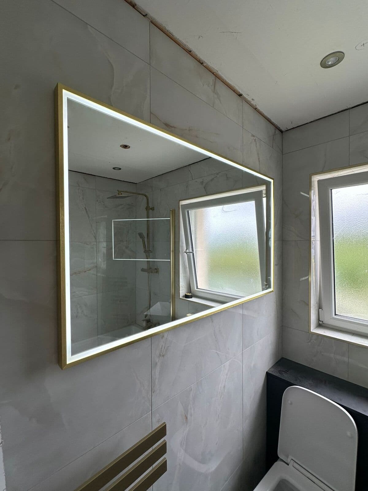 Large rectangular backlit mirror in a tiled bathroom