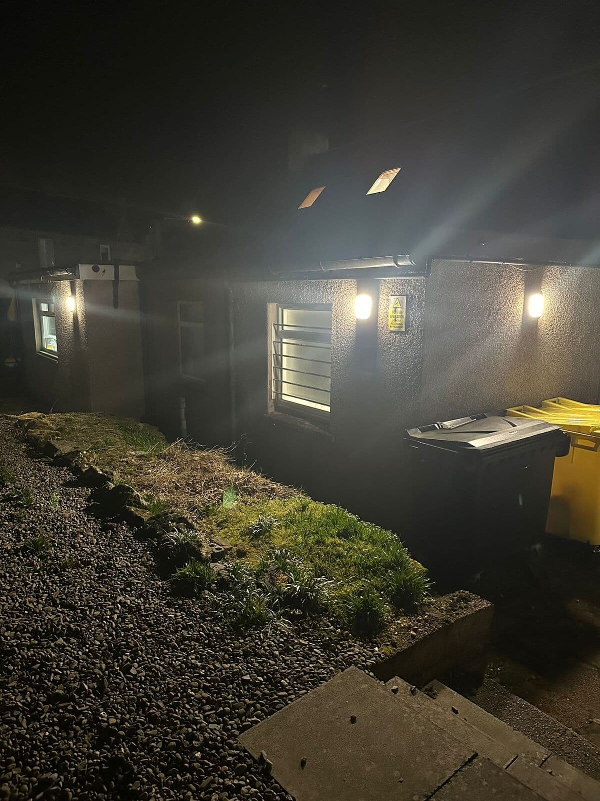 Outside wall lights lighting up a garden at night