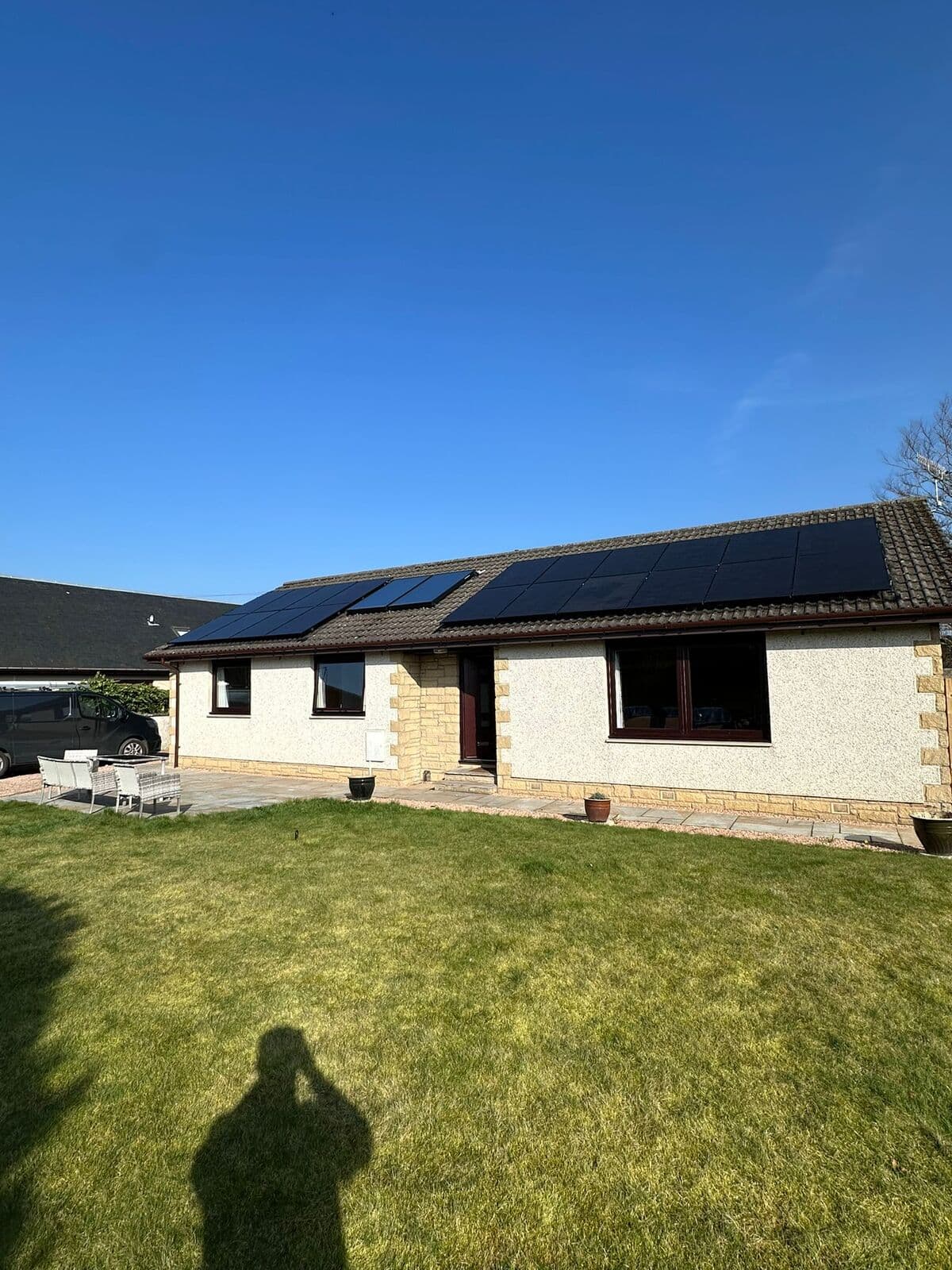 Solar panels on a bungalow roof with a green lawn in front