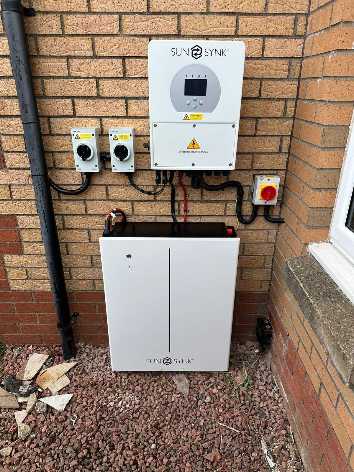 Sunsynk solar inverter with a home battery below on a brick wall